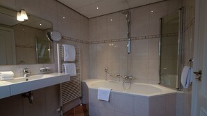 A modern bathroom with a large bathtub, a separate shower area, and a vanity with a mirror and sink. - Grand Hotel De Draak And Residence Dagmara (Bergen op Zoom)