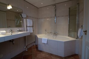 A modern bathroom with a large bathtub, a separate shower area, and a vanity with a mirror and sink. - Grand Hotel De Draak And Residence Dagmara (Bergen op Zoom)