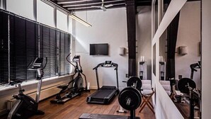 A home gym with exercise equipment, wooden floors, and a ceiling fan. - Grand Hotel De Draak And Residence Dagmara (Bergen op Zoom)