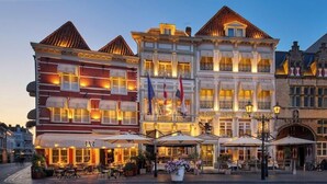 A historic hotel with a classic European facade, outdoor seating, and flags. - Grand Hotel De Draak And Residence Dagmara (Bergen op Zoom)