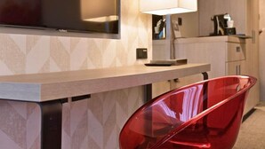 A modern kitchen area with a wooden countertop, a red chair, a lamp, and a coffee machine.