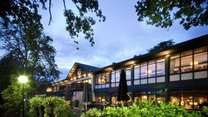 A modern hotel with a glass facade, outdoor seating, and lush greenery.