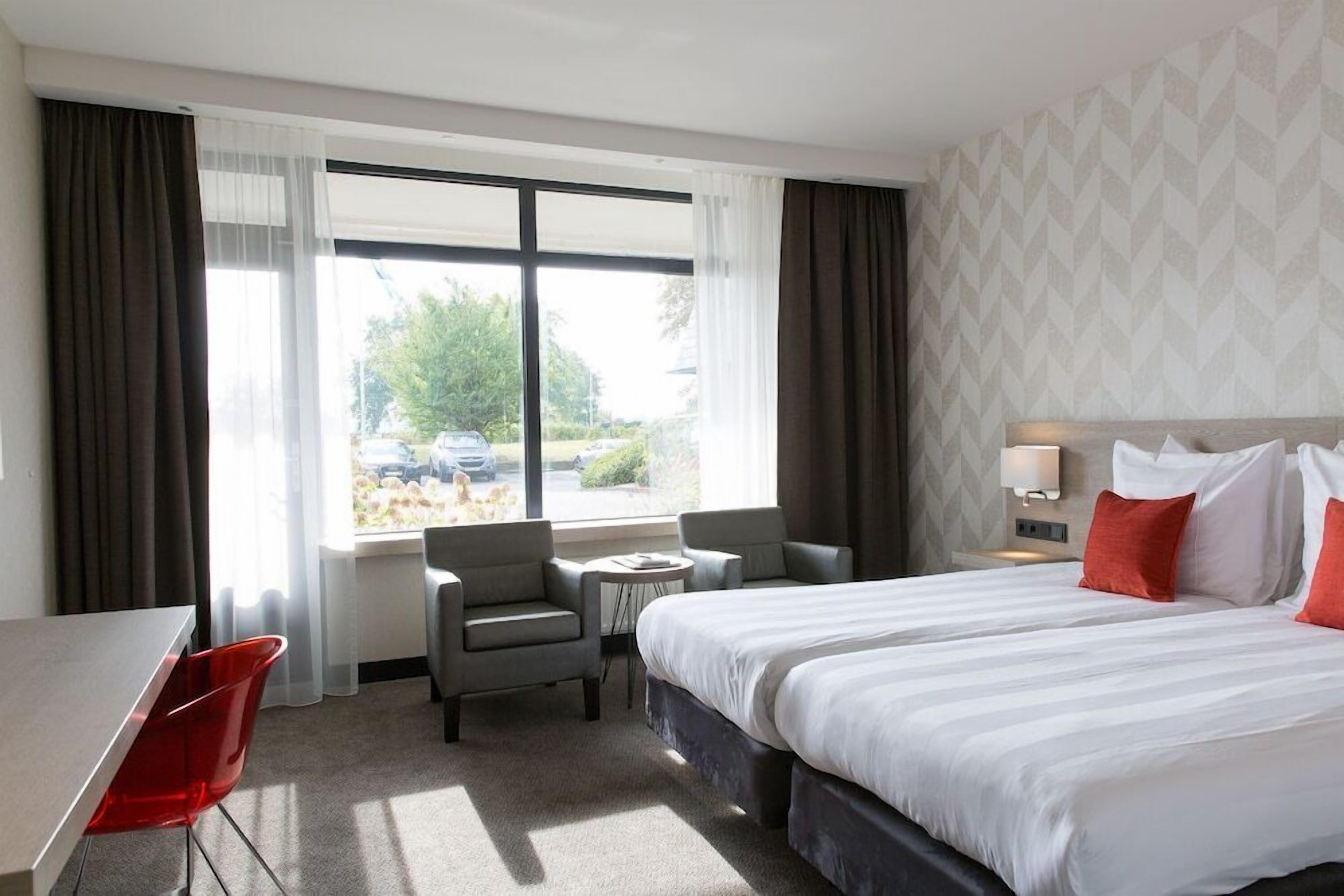 Ein Hotelzimmer mit einem großen Bett, zwei Sesseln, einem kleinen Tisch und einem Schreibtisch.