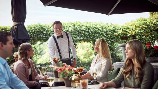 A group of people dining outdoors at a restaurant with a waiter serving them.