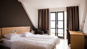Une chambre d’hôtel avec un lit, un bureau, une chaise et une fenêtre avec des rideaux.