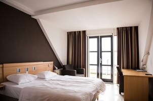 Una habitación de hotel con cama, escritorio, silla y ventana con cortinas.