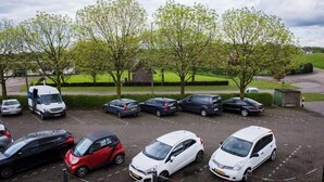 Un parking où sont garées différentes voitures, avec quelques arbres en arrière-plan.