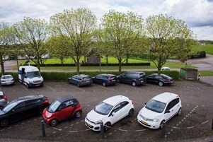 Un estacionamiento con varios coches y algunos árboles al fondo.