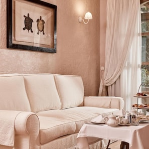 A beige sofa, a framed artwork, a wall-mounted light fixture, and a table with a tea set. - La Villa Del Re - Adults Only (Castiadas)