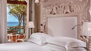 A bedroom with a large bed, a decorative headboard, and a view of the sea through an open archway. - La Villa Del Re - Adults Only (Castiadas)