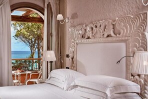 A bedroom with a large bed, a decorative headboard, and a view of the sea through an open archway. - La Villa Del Re - Adults Only (Castiadas)