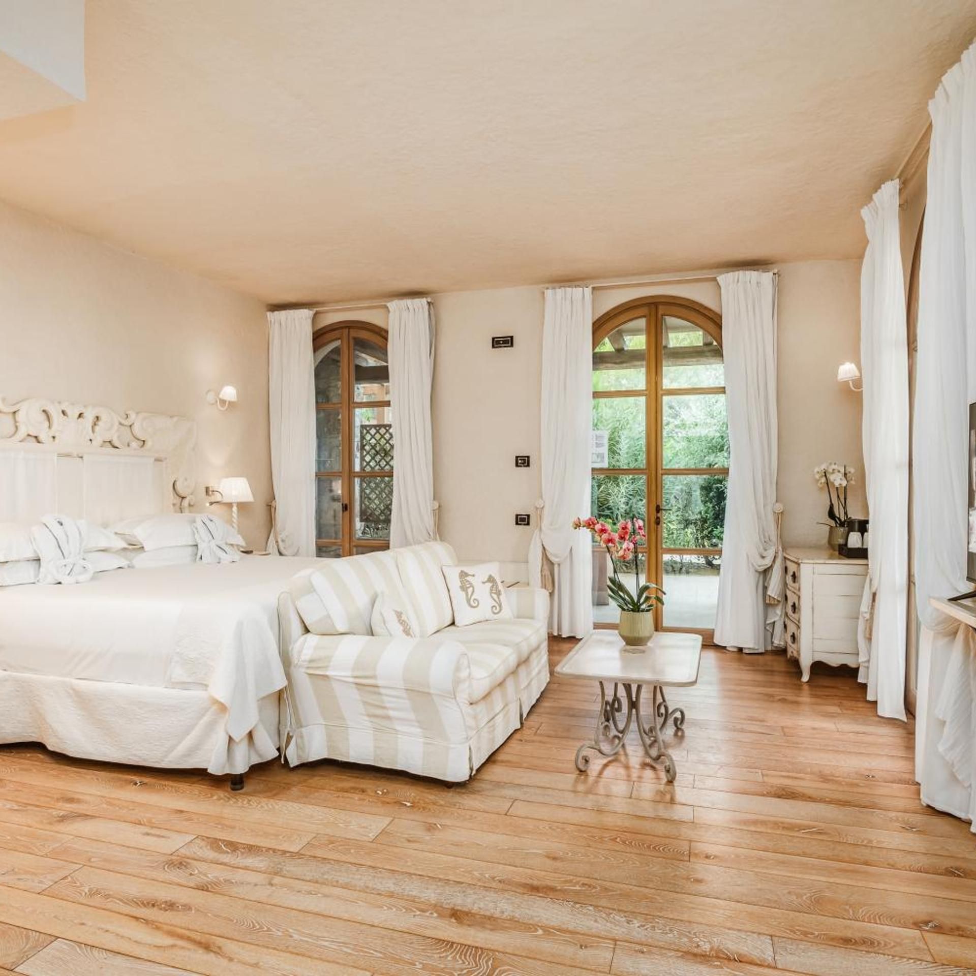 Una camera d'albergo con un letto, una poltrona, un tavolino e una finestra con tende.