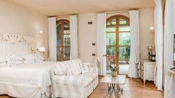 Una camera d'albergo con un letto, una poltrona, un tavolino e una finestra con tende.