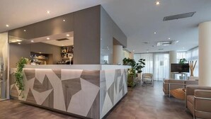 Una moderna zona de recepción con un mostrador de diseño geométrico, un área de descanso con sofás y una televisión.