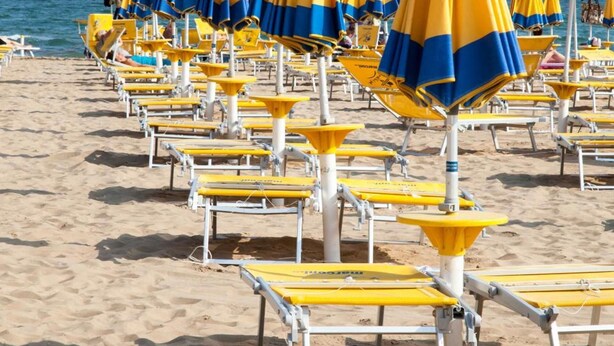 Una playa con hileras de sombrillas azules y amarillas a rayas y sillas de playa blancas.