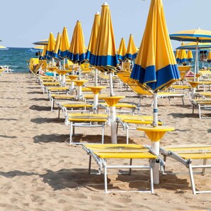 Una playa con hileras de sombrillas azules y amarillas a rayas y sillas de playa blancas.