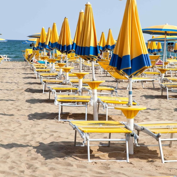 A beach with rows of yellow and blue striped umbrellas and white lounge chairs. - Hotel Rosanna 3 Stelle Superior (Jesolo)