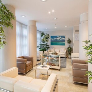 Una sala de estar moderna con una mesa de centro de vidrio, sofás color beige y un ventanal con cortinas.