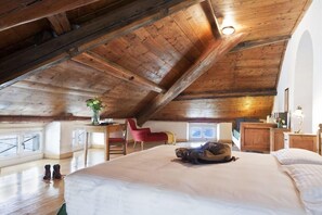 Un dormitorio amplio en el ático con un techo alto de madera, una cama grande, un escritorio y una silla roja.