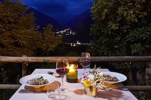 A table set outdoors with plates of food, wine glasses, and a candle, overlooking a mountainous landscape. - Hotel Bagni Vecchi (Valdidentro)