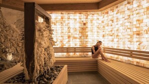 A sauna with a stone wall, wooden benches, and a rock feature. - Hotel Bagni Vecchi (Valdidentro)
