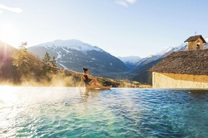 A person sitting in a clear pool with a mountain backdrop and a small building with a cross on top. - Hotel Bagni Vecchi (Valdidentro)