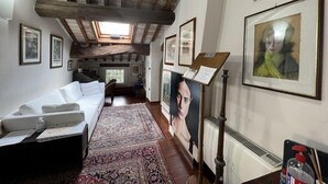 Une pièce avec un plafond en pente, des poutres en bois, un lit, un bureau, une chaise, une grande moquette et plusieurs œuvres d’art encadrées accrochées aux murs.
