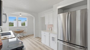 A modern kitchen with a stainless steel refrigerator, white cabinetry, a wooden dining table, and a window with curtains. - Relax at Stephens Legacy Farmhouse, a spacious 4BR retreat with valley and mountain views (Dayton)