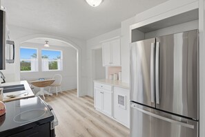A modern kitchen with a stainless steel refrigerator, white cabinetry, a wooden dining table, and a window with curtains. - Relax at Stephens Legacy Farmhouse, a spacious 4BR retreat with valley and mountain views (Dayton)