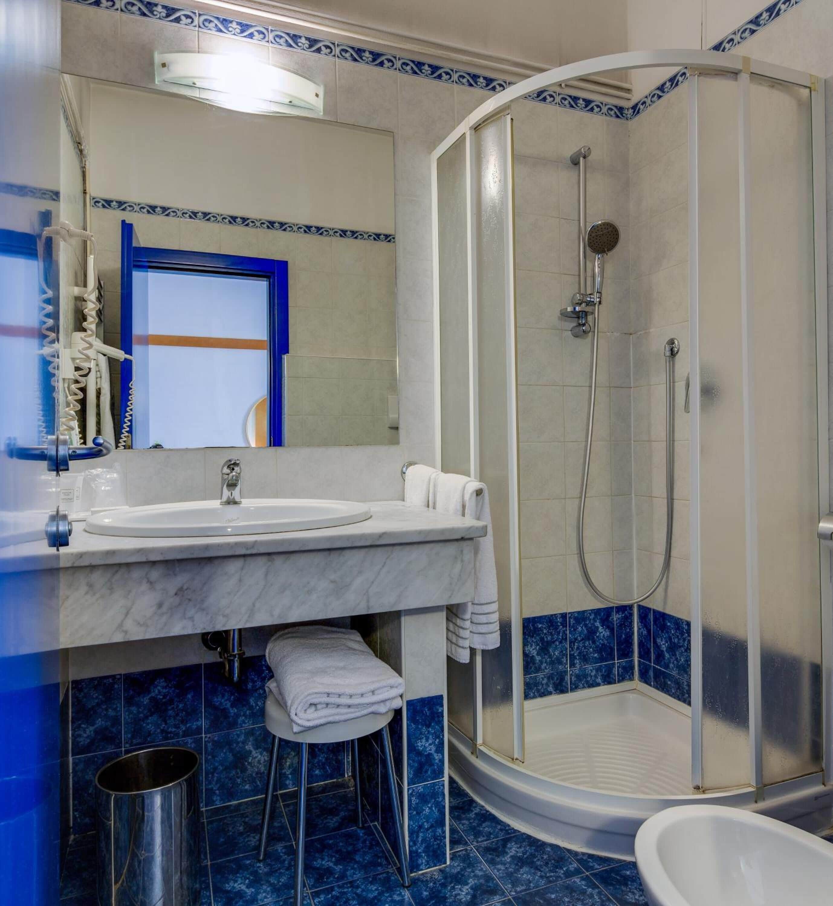 A bathroom with a white sink, a mirror, a shower with a glass door, and blue-tiled walls.