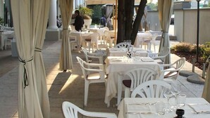 An outdoor dining area with white plastic chairs and tables, covered by a yellow canopy. - San Marco (Noceto)