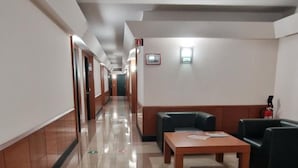 A hotel corridor with a tiled floor, wooden paneling on the walls, and a seating area with a table and chairs. - Mareschi Palace (Novara)