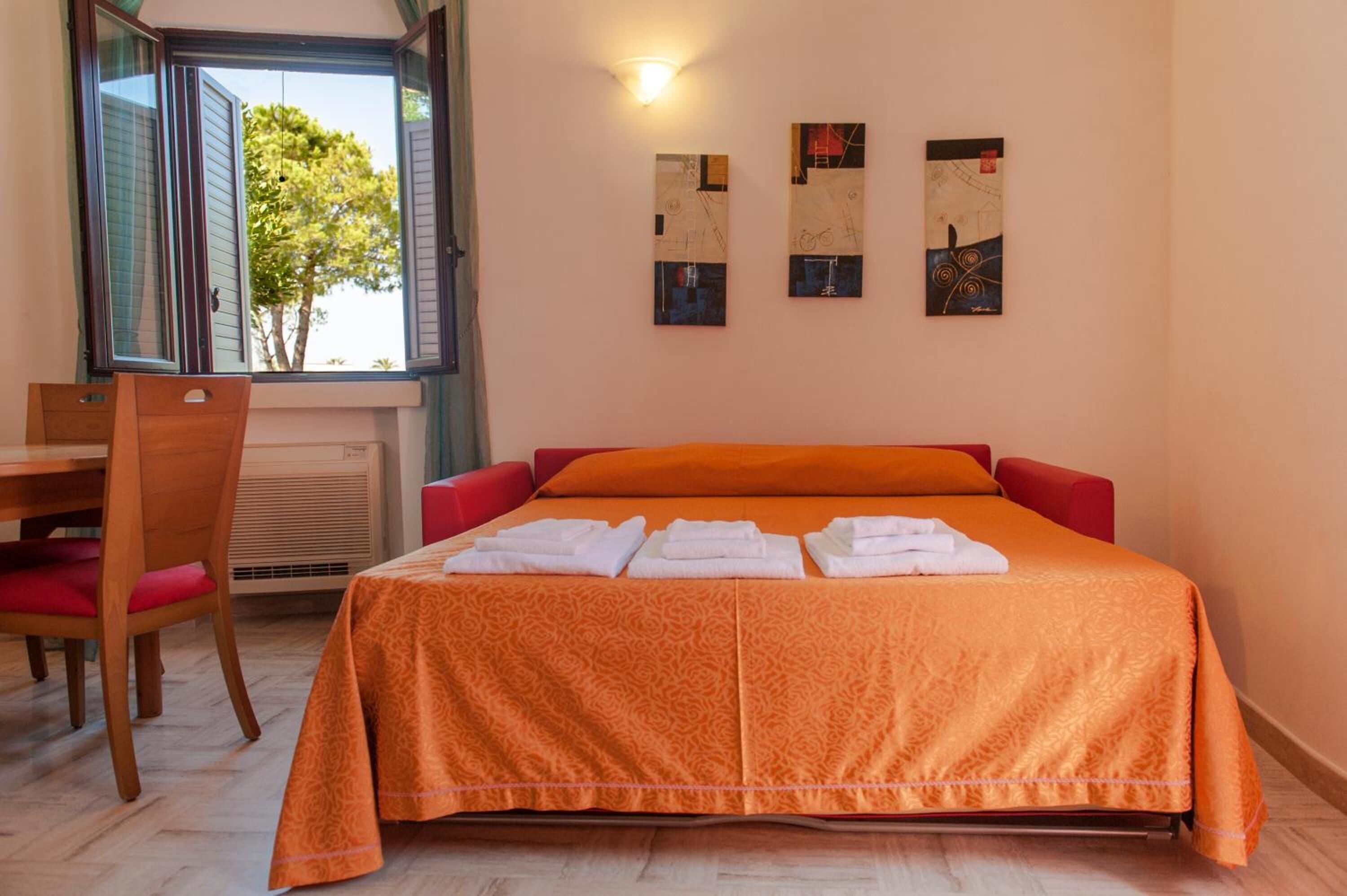 Ein Hotelzimmer mit Bett, Schreibtisch und Stühlen. Drei Gemälde hängen an der Wand.