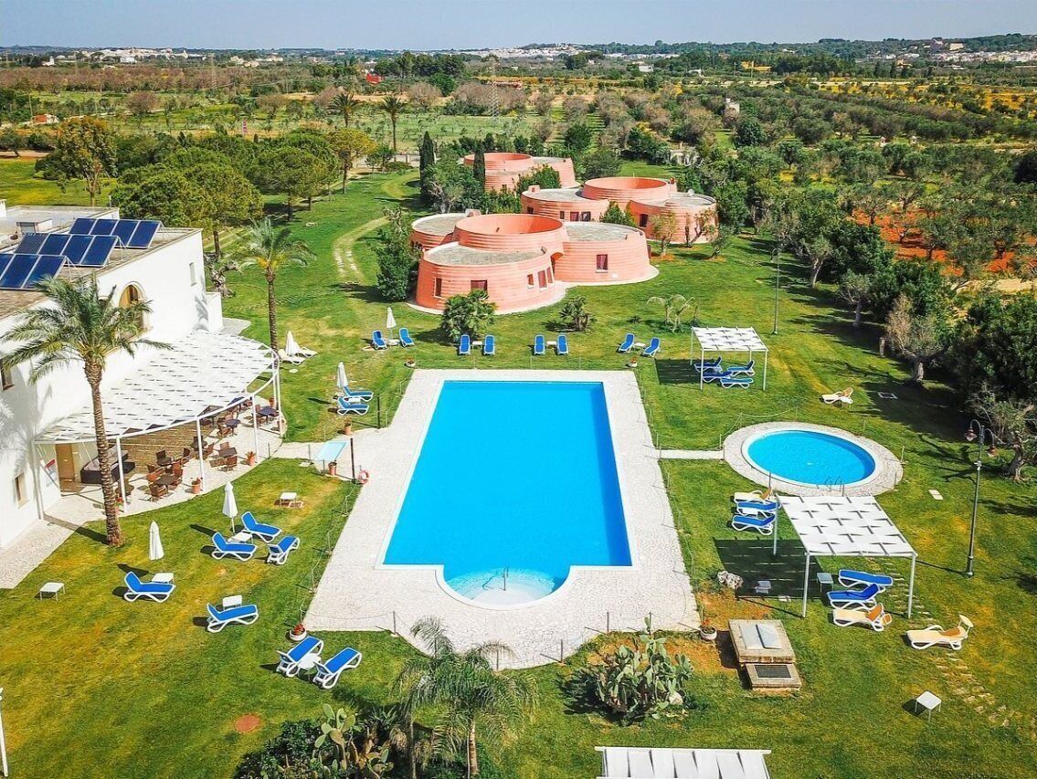 A resort with a large rectangular pool, multiple circular structures, and sun loungers.