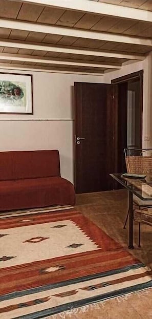 Une pièce avec un canapé rouge, un tapis à motifs, une porte en bois et une petite table avec une chaise.