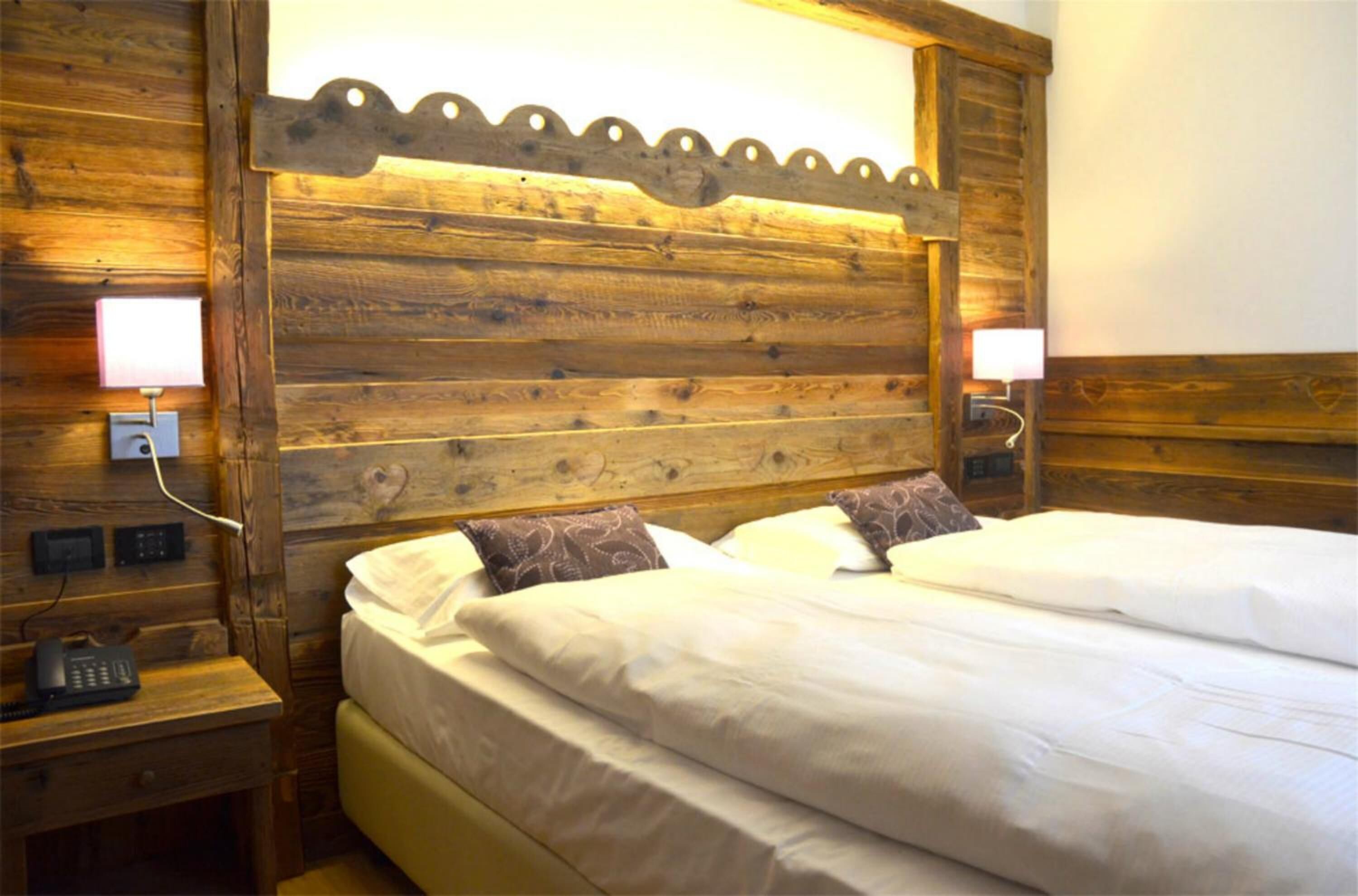 Cabecera de madera con diseño escarchado, cama con ropa blanca, dos lámparas de noche y un teléfono en la mesita.