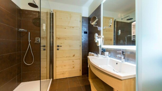 A modern bathroom with a glass shower enclosure, a wooden door, a large mirror, and a white sink. - Alp Holiday Dolomiti (Dimaro Folgarida)