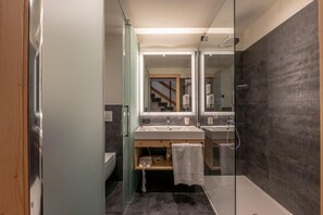 A modern bathroom with a glass shower enclosure, two sinks, a toilet, and a wooden vanity. - Alp Holiday Dolomiti (Dimaro Folgarida)
