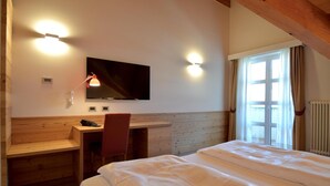 A hotel room with a bed, a desk, a chair, a TV mounted on the wall, and a window with curtains. - Alp Holiday Dolomiti (Dimaro Folgarida)