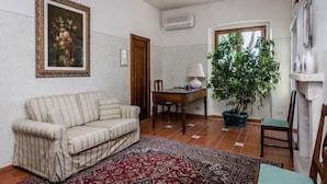 A living room with a striped sofa, a dining table with chairs, a potted plant, and a large window. - Relais Villa Acquaviva (Manciano)