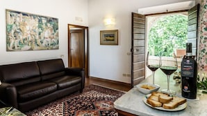 A living room with a leather sofa, a patterned rug, a painting, a wine bottle, and glasses on a table. - Relais Villa Acquaviva (Manciano)