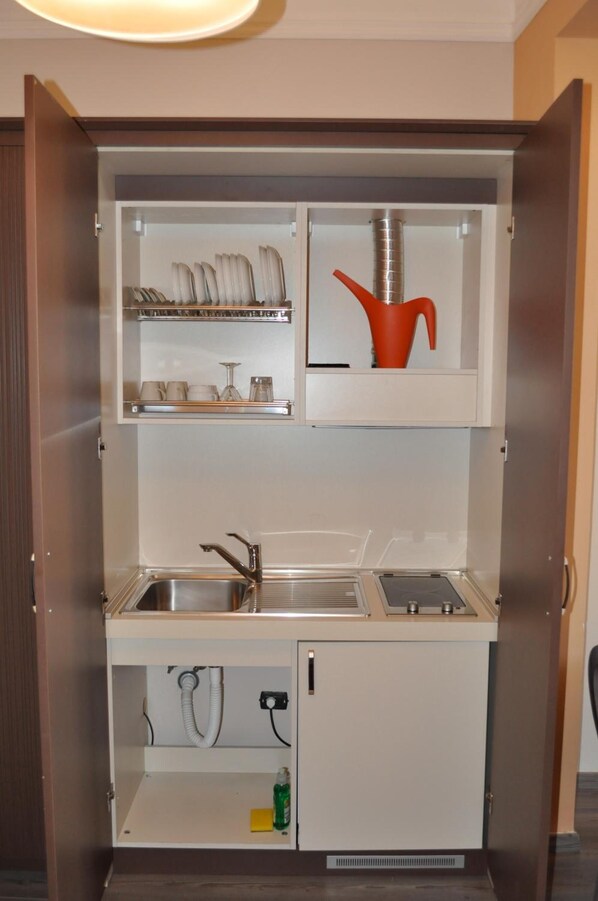 Eine kleine Küchenzeile mit Spüle, Geschirrgestell und einem kleinen Schrank mit einem roten Topf.