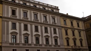 A multi-story building with a classical architectural style, featuring a central entrance with a portico and multiple balconies.
