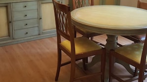 A dining area with a round table, wooden chairs, a television on a cabinet, and a door in the background.