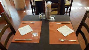 Une table dressée pour deux personnes, avec des sets de table, des couverts, des verres et un vase rempli de fleurs.