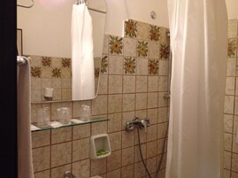 Un baño con ducha, repisas de vidrio con artículos de aseo y pared con azulejos con motivos florales.