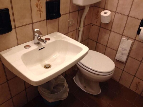 A bathroom with a sink and toilet, a trash bin, and a paper towel dispenser. - Hotel Europa (Rovigo)