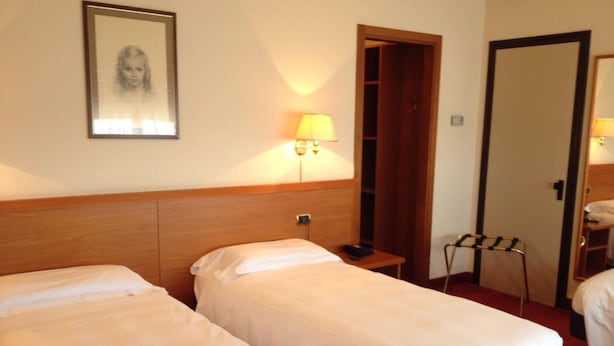 Une chambre d’hôtel avec deux lits, une table de chevet, une lampe, une porte et un tableau encadré au mur.