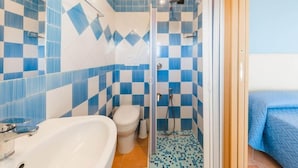 A bathroom with a white sink, toilet, and shower. The walls are tiled with blue and white checkered patterns. - Albergo La Margherita (Scala)