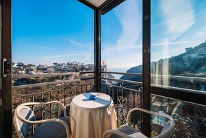 Un balcón con mesa y sillas, con vistas a un pueblo costero y acantilados.